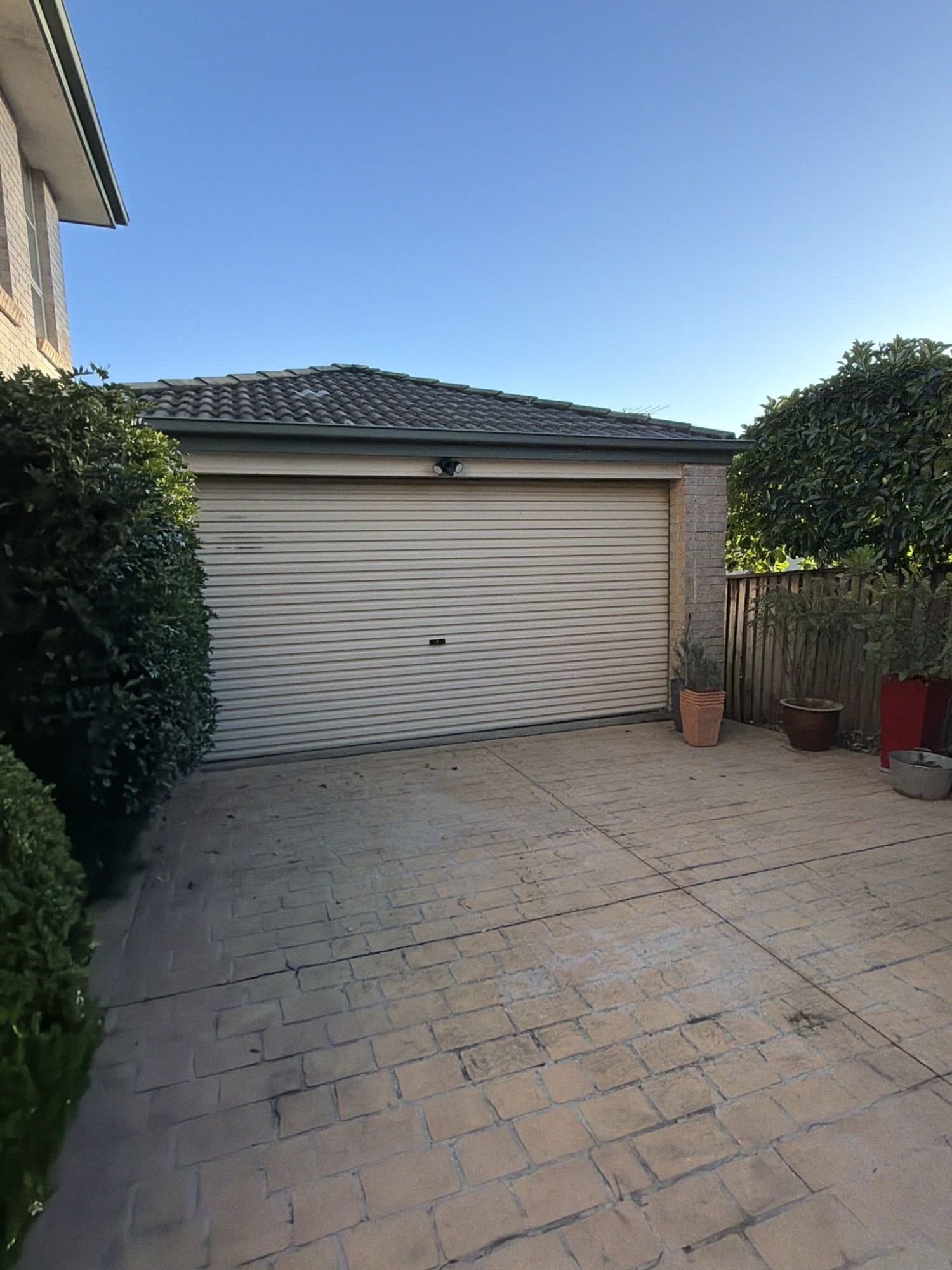 A paved driveway in front of a cream roller-door garage, before the work.